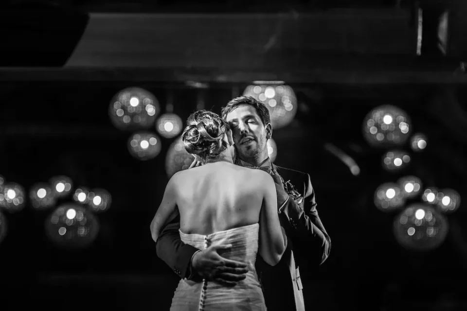 Première danse des mariés en noir et blanc à la Ferme des Templiers de Verlinghem. Le marié, les yeux fermés, profite de l’instant, entouré de la lumière des lustres. Photo capturée par Christophe Blaszkowski, photographe de mariage sur Lille.