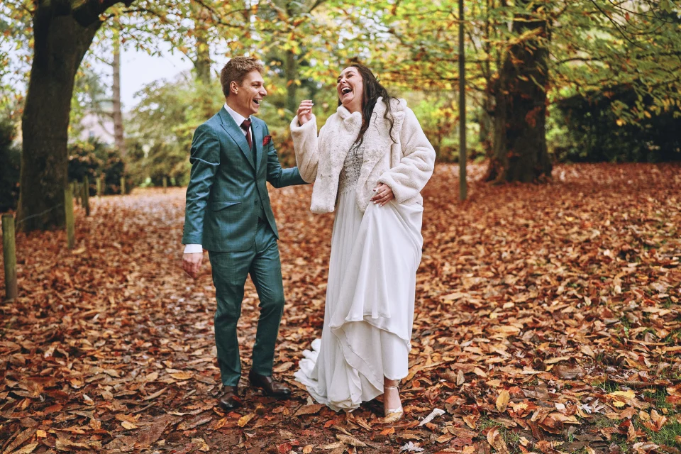 Photo de couple des mariés en forêt dans l'Aisne pendant l'automne, riant ensemble parmi les feuilles mortes. Photographe d'événements de mariage à Lille.