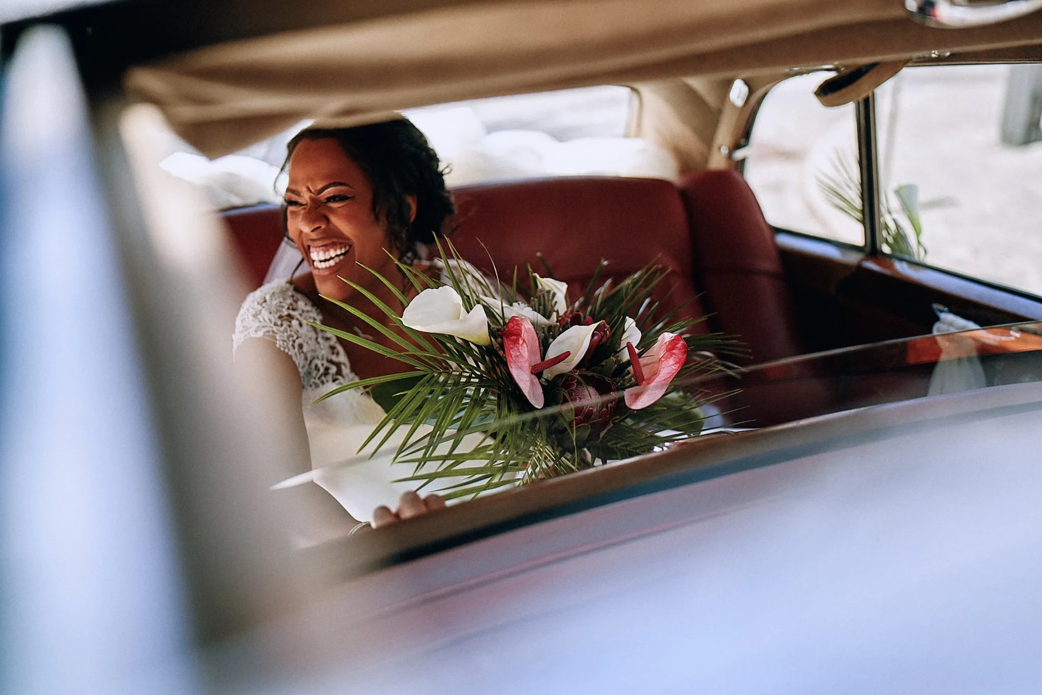 Mariée souriante, regardant ses invités à travers le pare-brise d'une voiture de type Traction, avec son bouquet en main. Photo de mariage par Christophe Blaszkowski, Professionnel de la photo de mariage et d’événements. Les mariés sont de rouvroy.