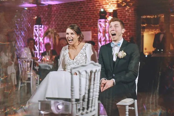 Les mariés de Saint Pol sur Ternoise riant aux éclats en découvrant un diaporama préparé par leurs invités. Photo de mariage par Christophe Blaszkowski, Photographe créatif pour vos photos de mariage sur Lille.