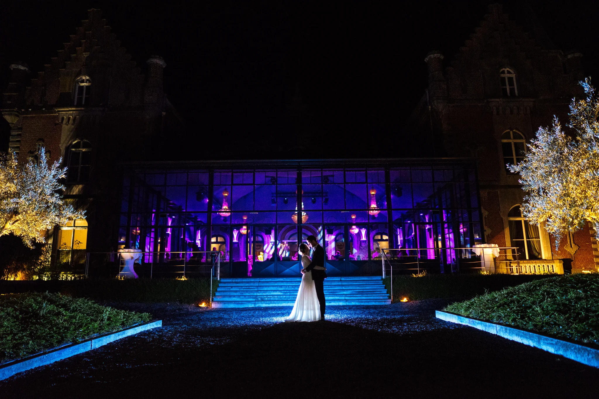 Photo de nuit des mariés devant la verrière illuminée du Château de Bourgogne à Estaimbourg. Atmosphère romantique et élégante. Photographe de mariage : Christophe Blaszkowski, Lille. Les mariés sont de Senlis.