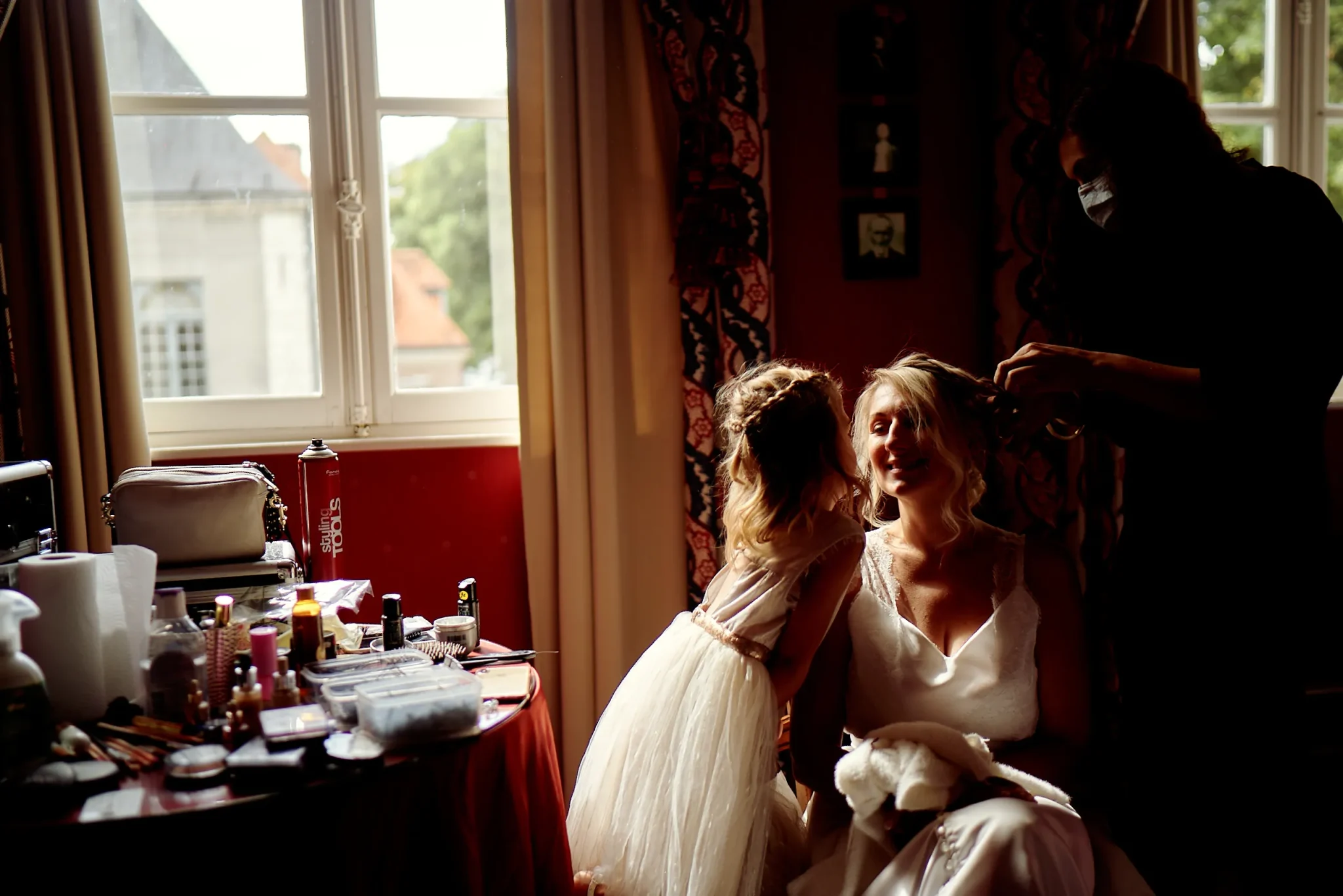 Regard complice entre la mariée et sa fille pendant les préparatifs de coiffure, sous les rayons de soleil au Domaine de la Chartreuse à Gosnay. Photo de mariage par Christophe Blaszkowski, Photographe expérimenté pour un mariage parfait sur le secteur de Lille.