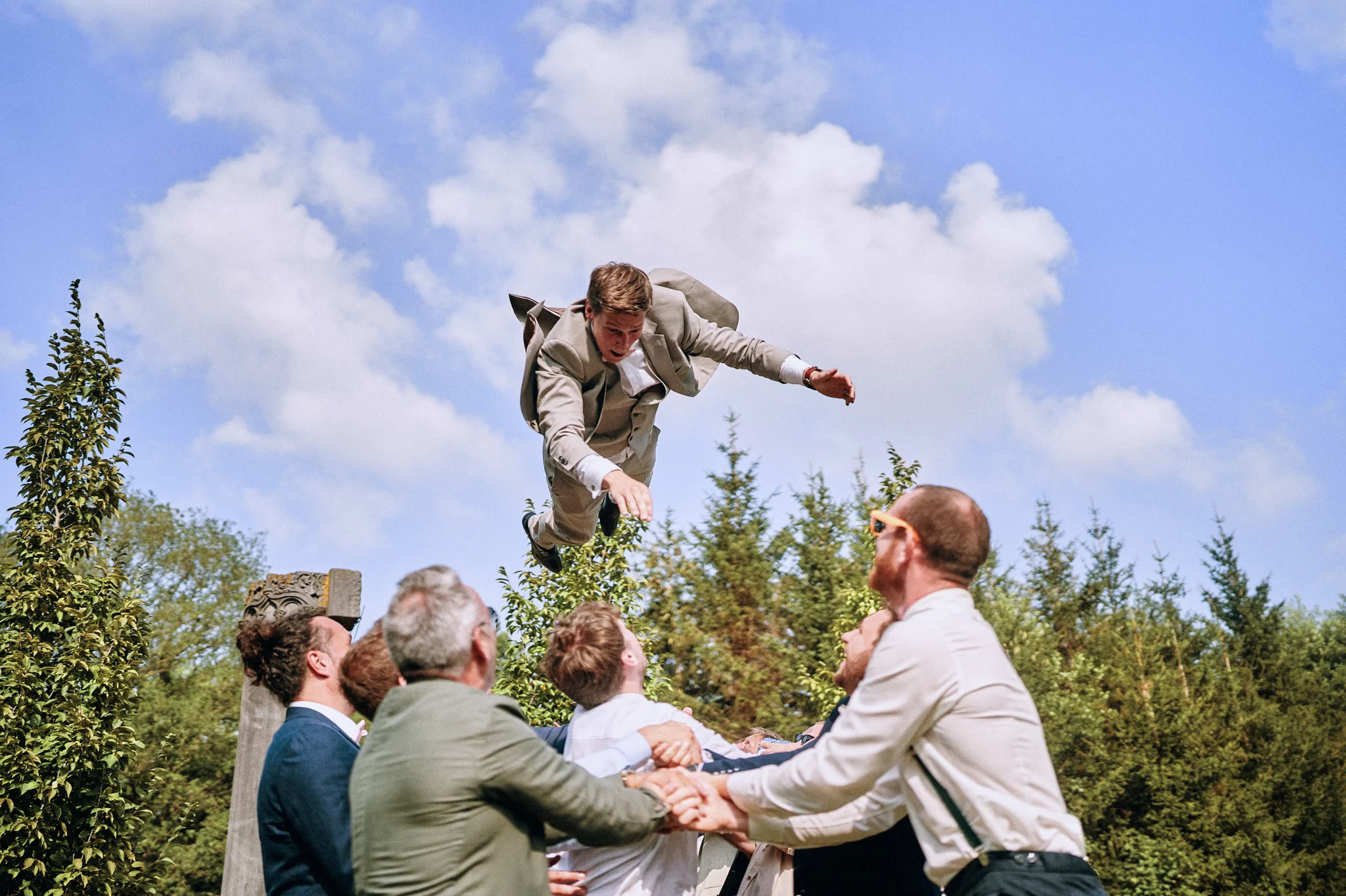 Marié de Mons lancé en l'air par ses témoins lors du vin d'honneur. Photo dynamique et pleine de rires capturée par Christophe Blaszkowski, photographe de mariage à Lille.