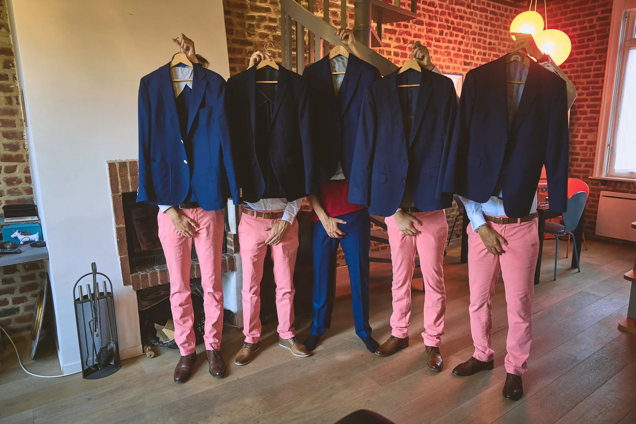 Préparatifs du marié avec ses témoins dans une photo humoristique. Tous cachent leur visage avec leur veste de costume et tiennent leurs parties intimes de l’autre main. Les témoins portent un pantalon rose et le marié un pantalon bleu. Photographe de mariage à Lille : Christophe Blaszkowski.
