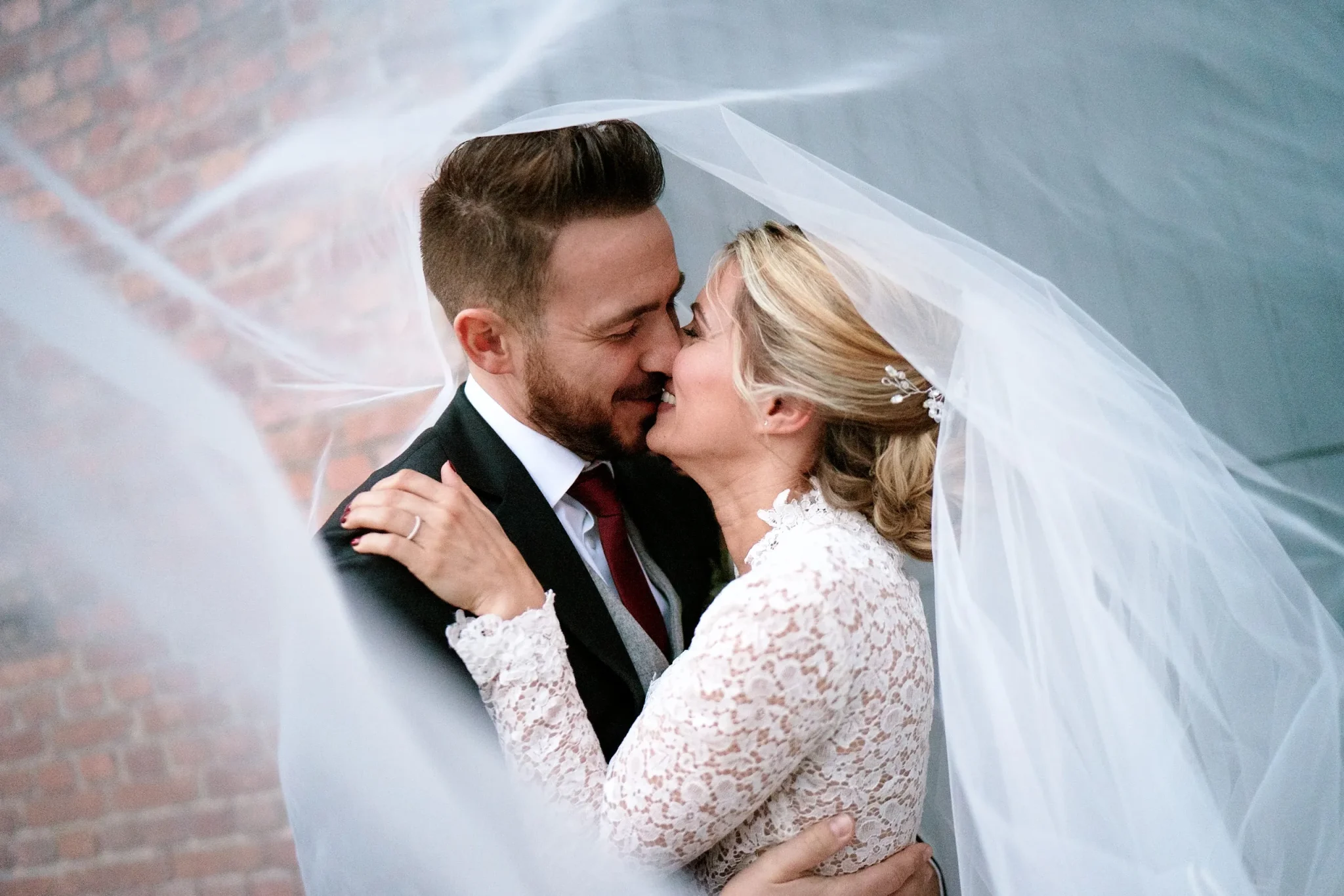 Couple de mariés souriant sous le voile de la mariée – photo naturelle prise à la Ferme des Templiers de Verlinghem, près de Lille.