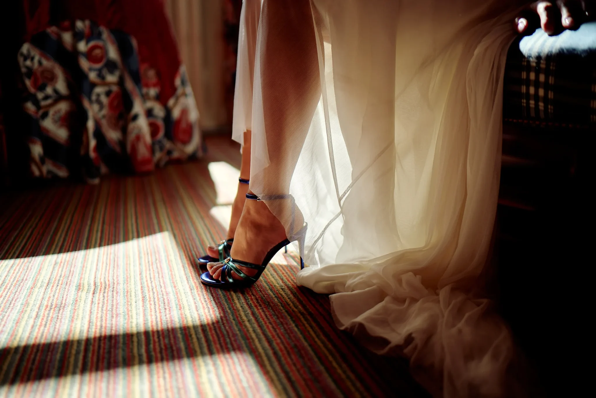 Détail des chaussures et des jambes de la mariée, avec sa robe, sous la lumière naturelle dans la chambre. Photo de mariage par Christophe Blaszkowski, Photographe de mariage dans la région de Lille.