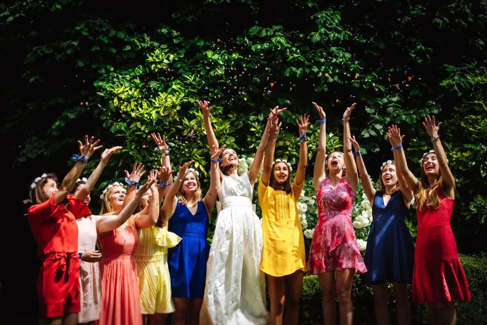 Photo de groupe de la mariée et ses témoins lançant des confettis colorés, dans un cadre naturel. Sourires, complicité et explosion de couleurs. Photographe de mariage : Christophe Blaszkowski, basé à Lille.
