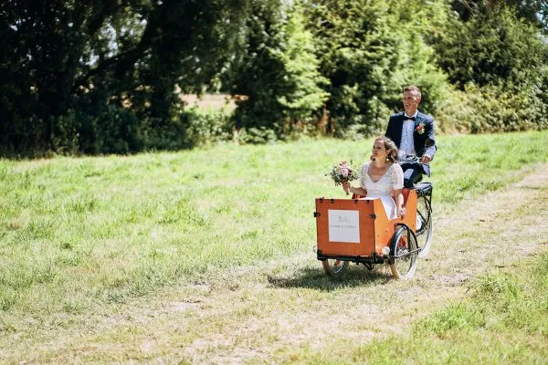 Les mariés de Bruay-la-Buissière arrivant à leur cérémonie laïque dans un tricycle, roulant sur un chemin de prairie. Photo de mariage par Christophe Blaszkowski, photographe de mariage sur Lille.